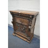 AN EARLY 20TH CENTURY FRENCH OAK SINGLE DOOR CABINET, carved with various masks that are flanking