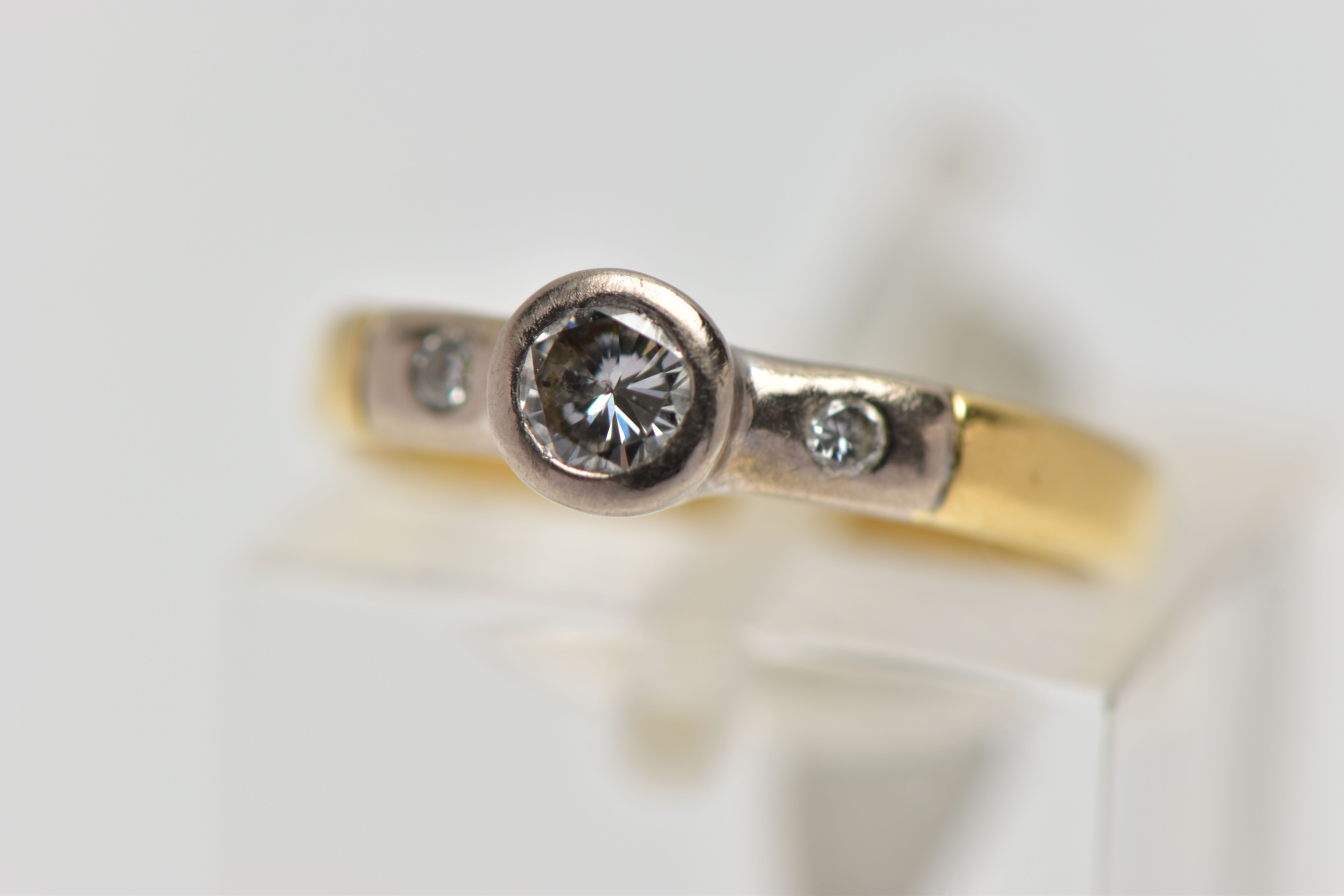 AN 18CT YELLOW GOLD DIAMOND RING, a single cut diamond bezel set in white gold, accented with two