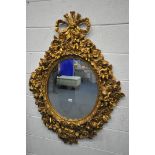 A 20TH CENTURY GILT OVAL WALL MIRROR, depicting a ribbon surmount, nine putto's with instruments,