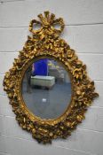 A 20TH CENTURY GILT OVAL WALL MIRROR, depicting a ribbon surmount, nine putto's with instruments,