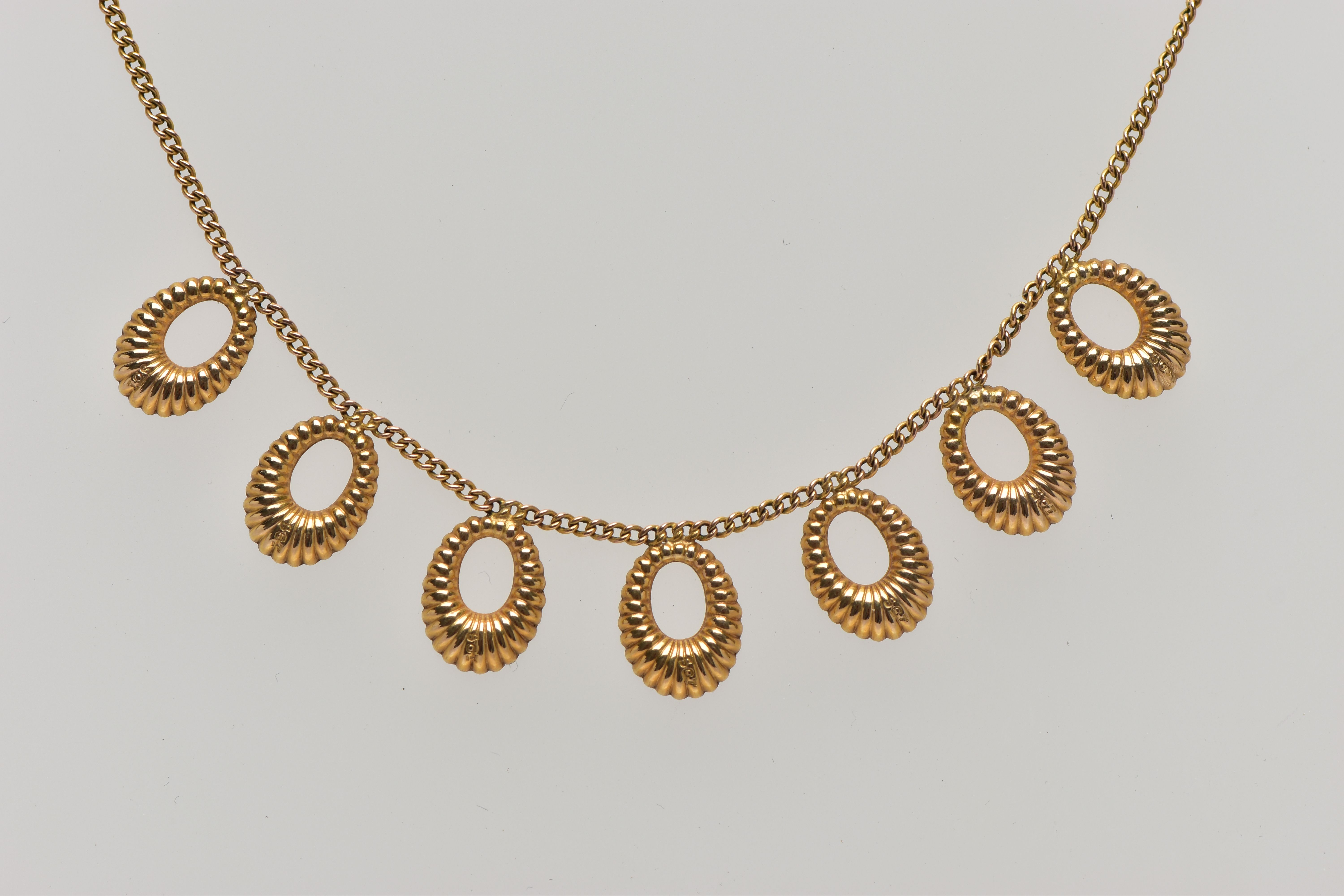 A YELLOW METAL FRINGE NECKLACE, comprising seven textured hoops, suspended from a flat curb link