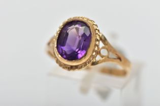 A 9CT GOLD AMETHYST SINGLE STONE RING, the oval cut amethyst collet set, within a rope twist