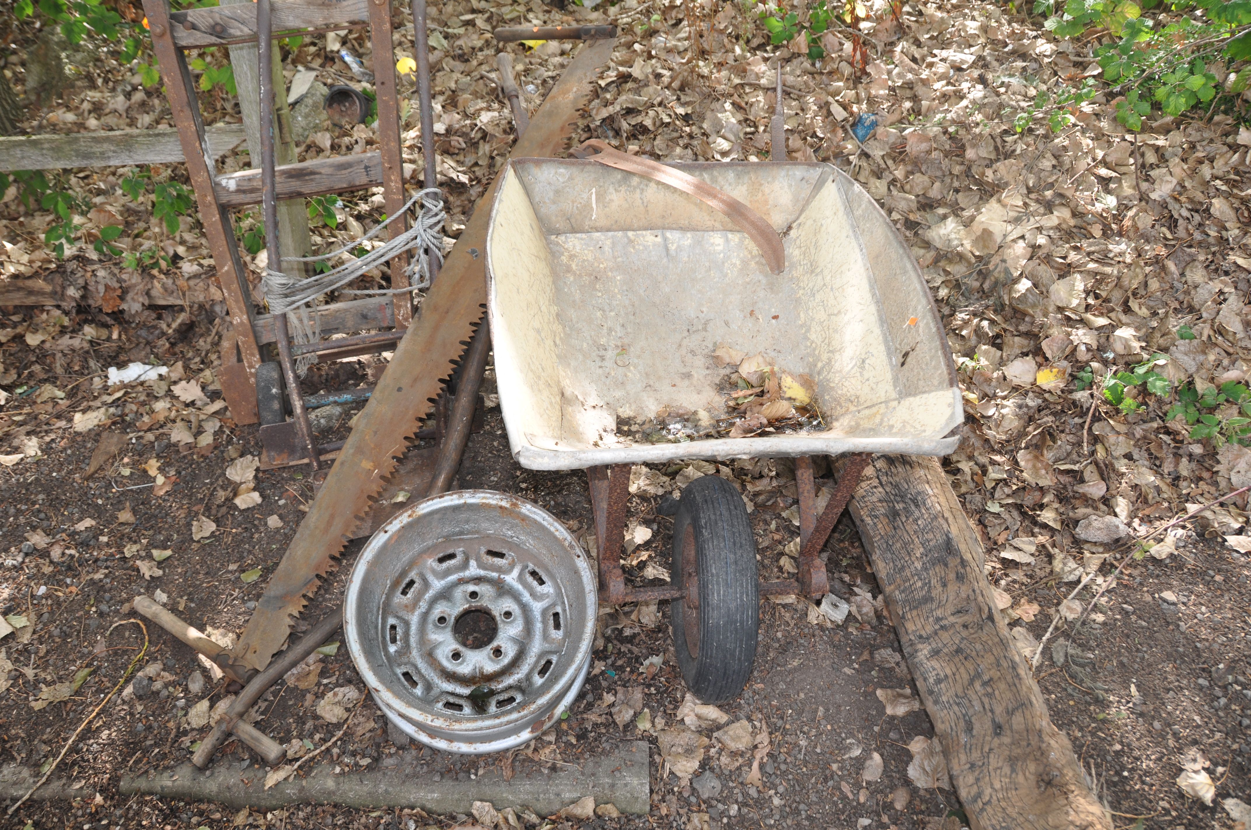 A SEVERLY WEATHERED VINTAGE WOODEN BEAM, a builders wheel barrow, two vintage sack trucks, a vintage