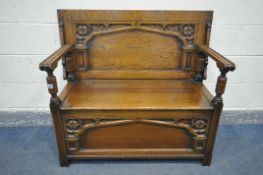 A 20TH CENTURY OAK MONKS BENCH, having a hinged lid and storage compartment, and a carved Gothic