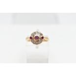 A 14CT GOLD RUBY AND DIAMOND RING, designed with a central circular cut ruby collet set, flanked