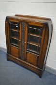 A MID CENTURY OAK GLAZED TWO DOOR BOOKCASE, the doors flanking a carved foliate section, above