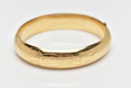 A YELLOW METAL BANGLE, a foliage engraved, hollow yellow metal oval hinged bangle, fitted with a