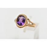 A 9CT GOLD AMETHYST SINGLE STONE RING, the oval cut amethyst collet set, within a rope twist