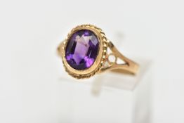 A 9CT GOLD AMETHYST SINGLE STONE RING, the oval cut amethyst collet set, within a rope twist