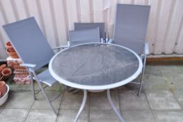 A METAL FRAMED AND SMOKED GLASS GARDEN TABLE diameter 100cm and four similar folding chairs (