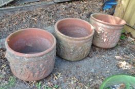 A SET OF THREE TERRACOTTA PLANT POTS with lion mask and cherub detailing 41cm in diameter and 36cm