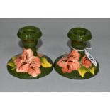 A PAIR OF MOORCROFT POTTERY DWARF CANDLESTICKS, coral 'Hibiscus' pattern on green ground, partial