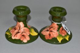 A PAIR OF MOORCROFT POTTERY DWARF CANDLESTICKS, coral 'Hibiscus' pattern on green ground, partial