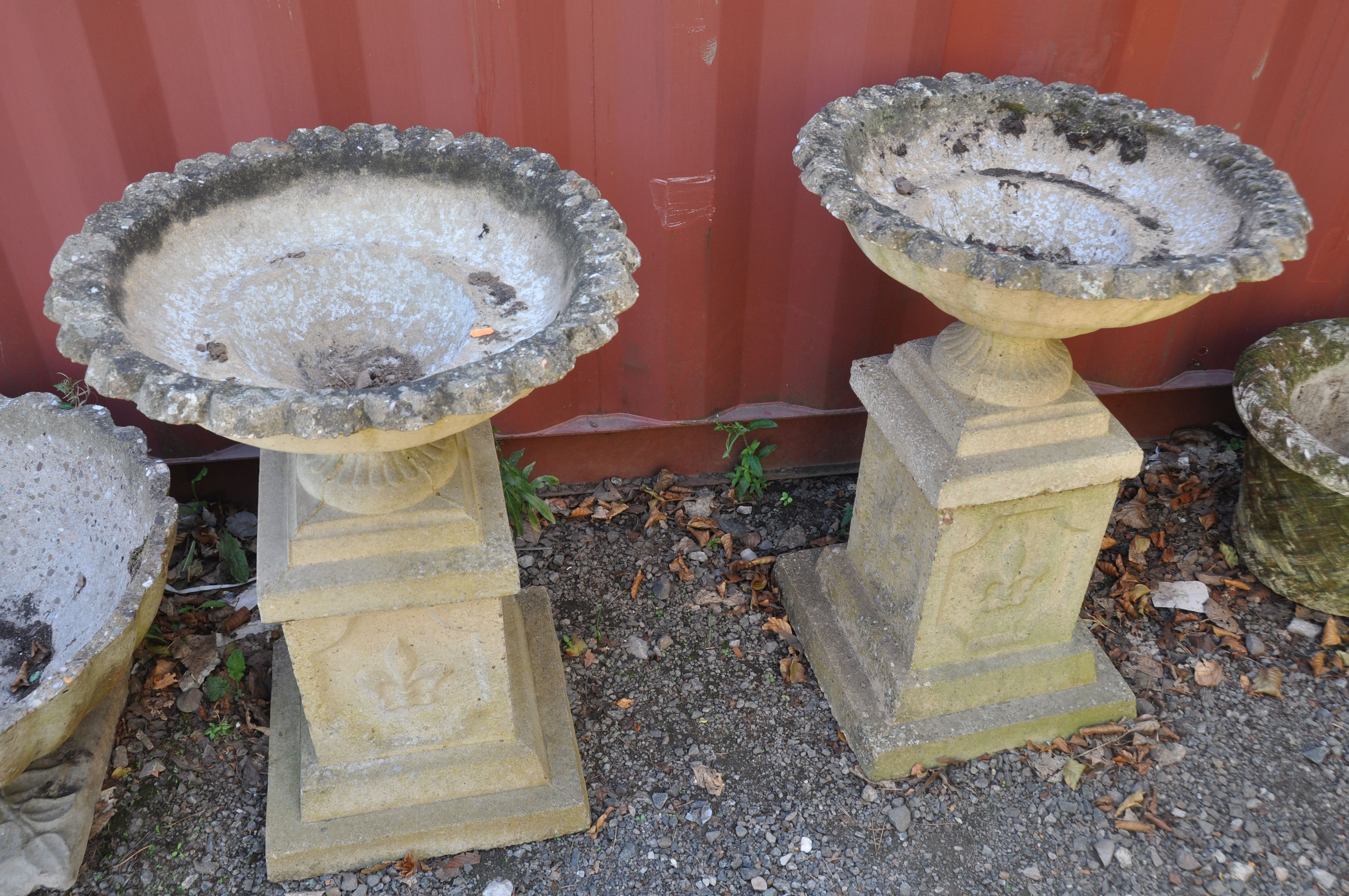 A PAIR OF MODRN COMPOSITE GARDEN URNS on square columns with pie crust top edges, baluster and