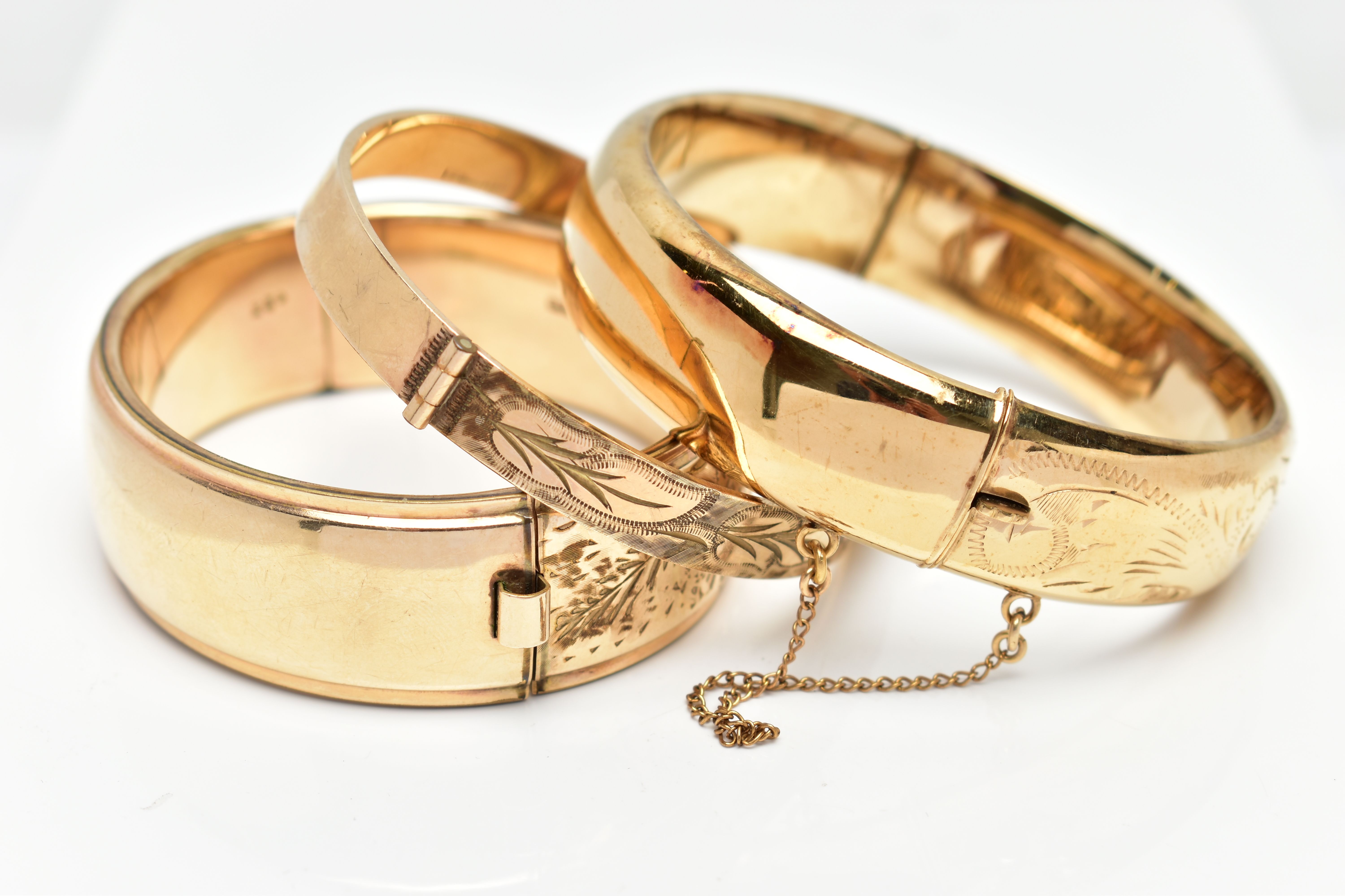 THREE YELLOW METAL HINGED BANGLES, each with a textured and engraved foliate panel design, to the - Image 2 of 3