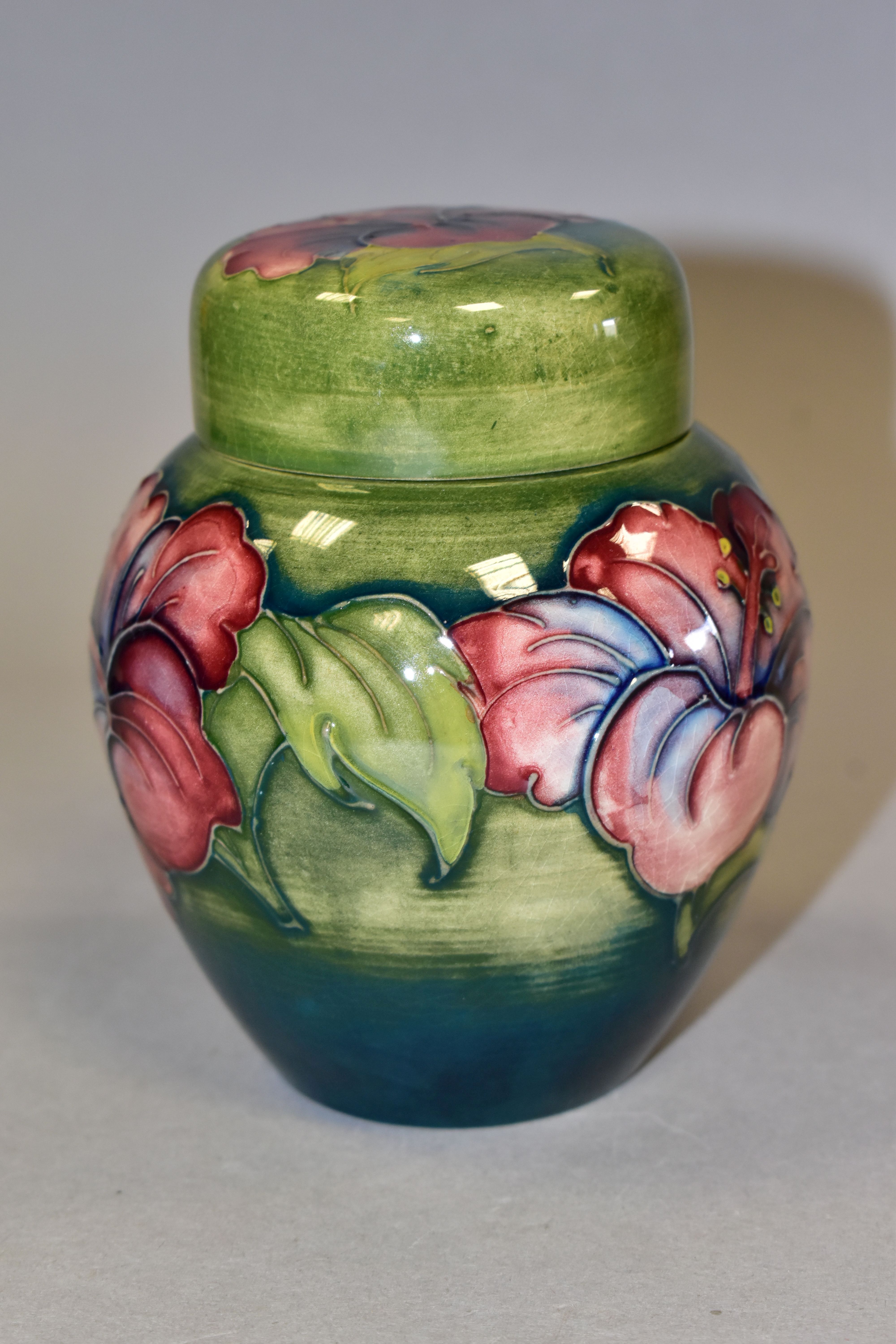 A MOORCROFT POTTERY HIBISCUS PATTERN COVERED GINGER JAR, the green ground decorated with pink,