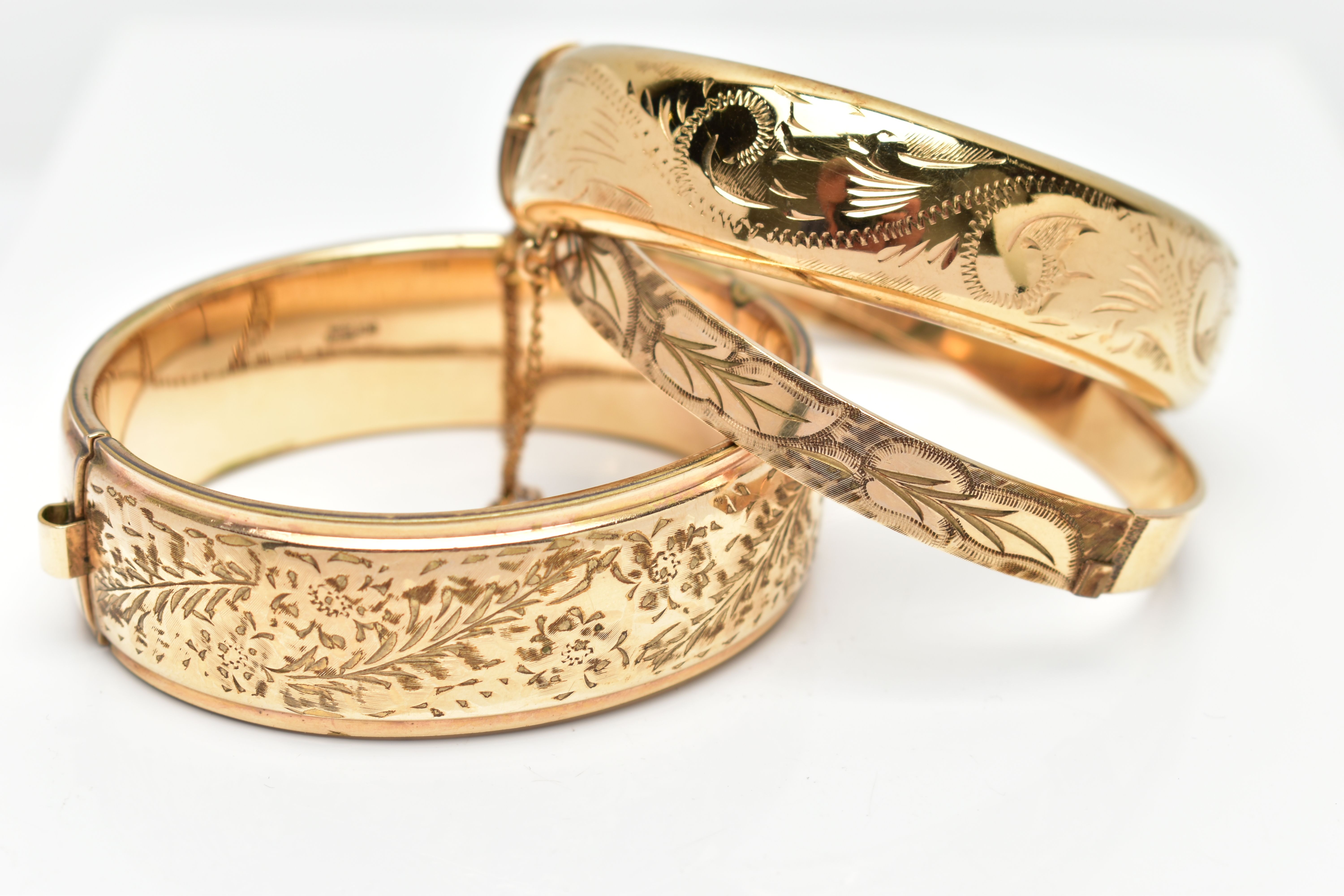 THREE YELLOW METAL HINGED BANGLES, each with a textured and engraved foliate panel design, to the