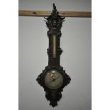 A VICTORIAN OAK WHEEL BAROMETER, the frame with a carved mask of a boy, and leaf scrolls and