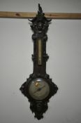 A VICTORIAN OAK WHEEL BAROMETER, the frame with a carved mask of a boy, and leaf scrolls and