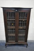 AN EARLY 20TH CENTURY ARTS AND CRAFTS TWO DOOR LEAD GLAZED BOOKCASE, with a shaped top, on