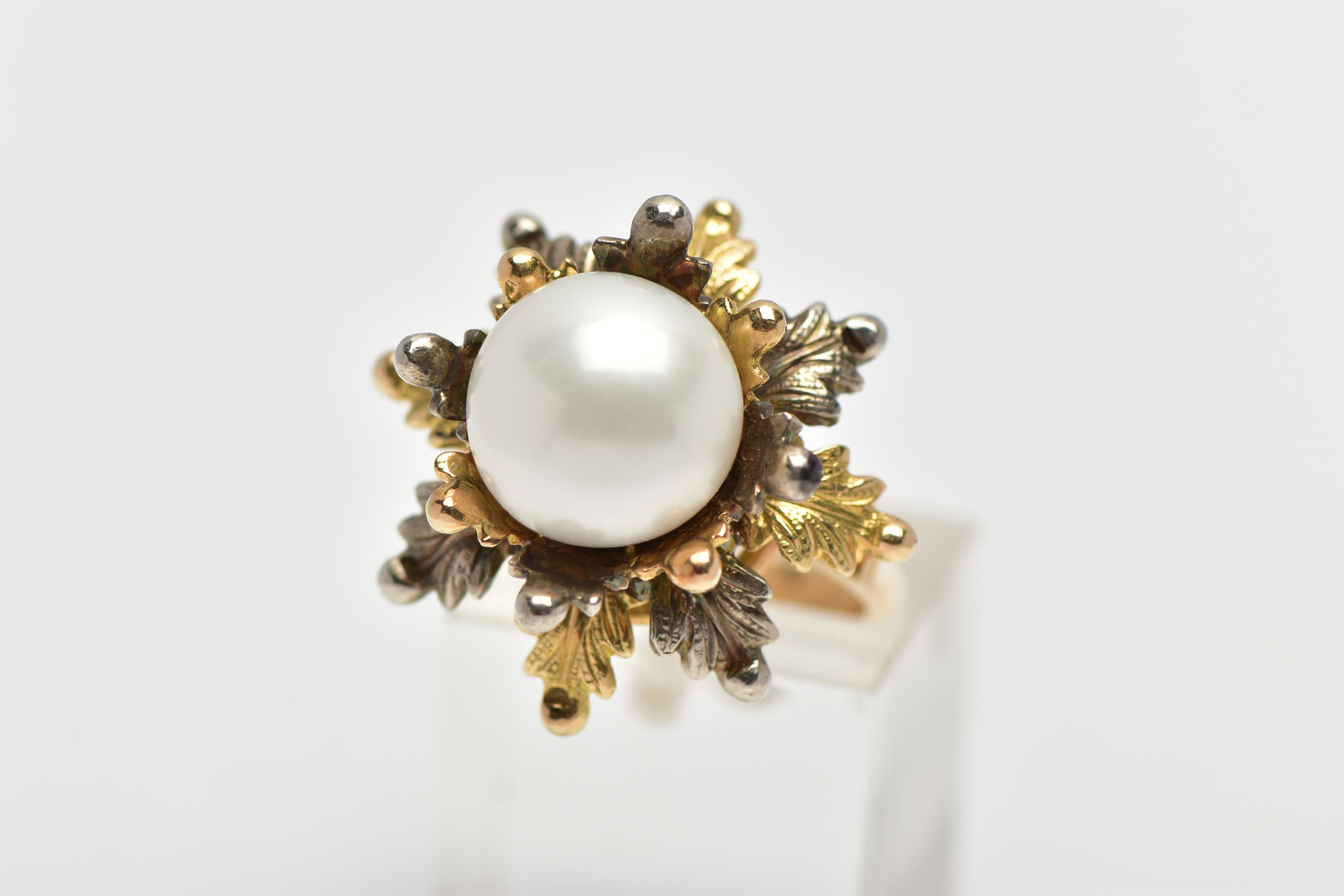 A WHITE AND YELLOW METAL CULTURED PEARL RING, of foliate design, set with a principal part drilled