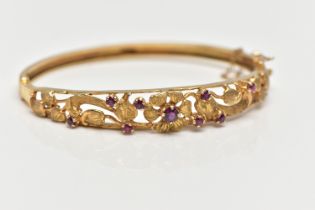 A 9CT GOLD FLORAL BANGLE, a yellow gold oval form hinged bangle, open work textured detail set