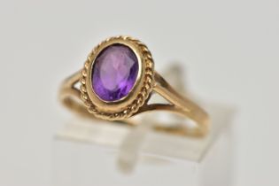 A 9CT GOLD AMETHYST SINGLE STONE RING, the oval cut amethyst within a collet setting, to the