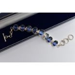A SILVER IOLITE BRACELET, the oval cut iolites collet set, with hinged spacers, to the circular link