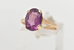 A YELLOW METAL AMETHYST RING, an oval cut amethyst four claw set in a yellow metal mount, polished