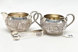 A WHITE METAL SUGAR BOWL, CREAMER AND PAIR OF SUGAR TONGS, the sugar bowl and creamer each decorated