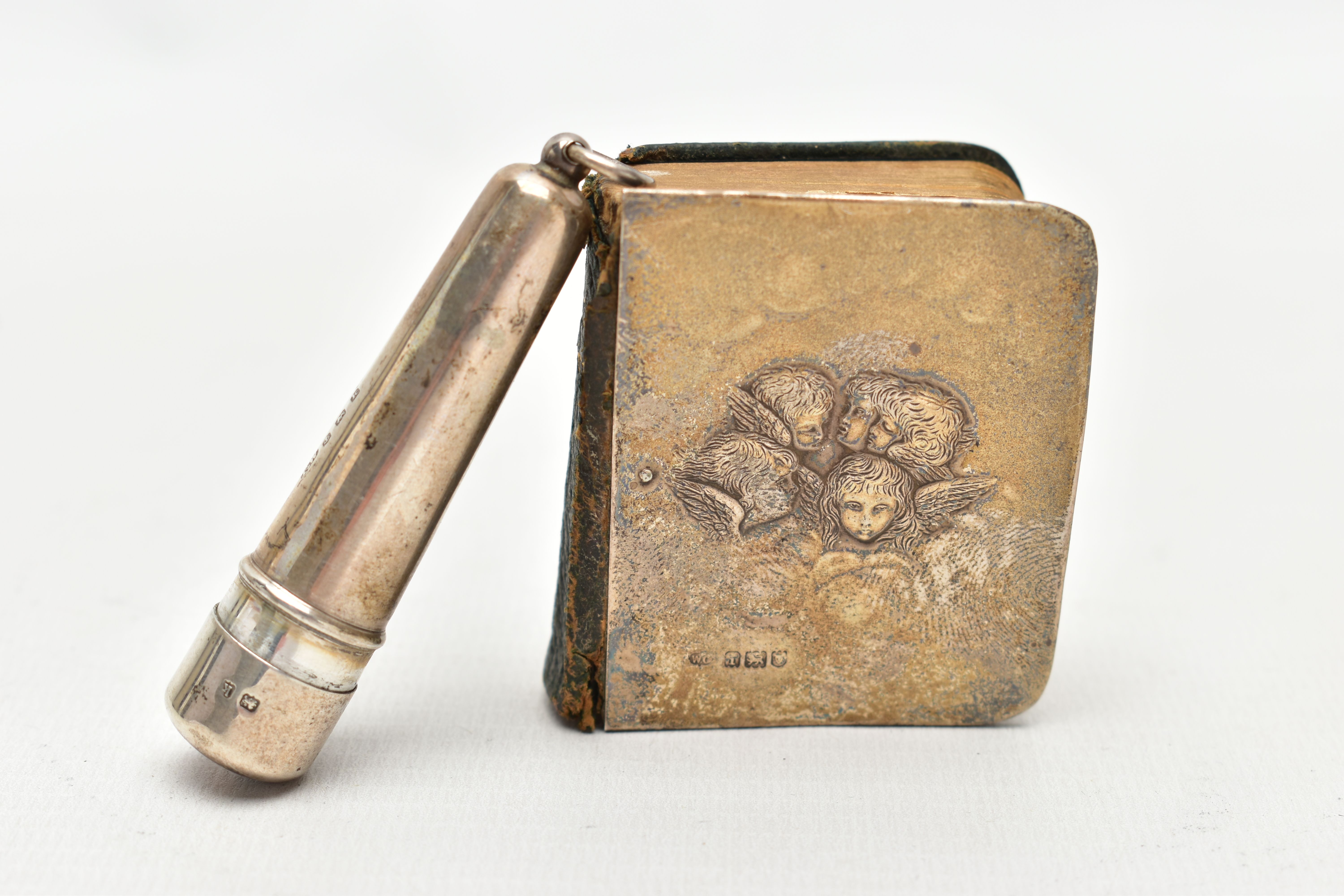 A SILVER PRAYER BOOK AND CIGAR HOLDER, the book with silver front panel depicting five Cherubs,