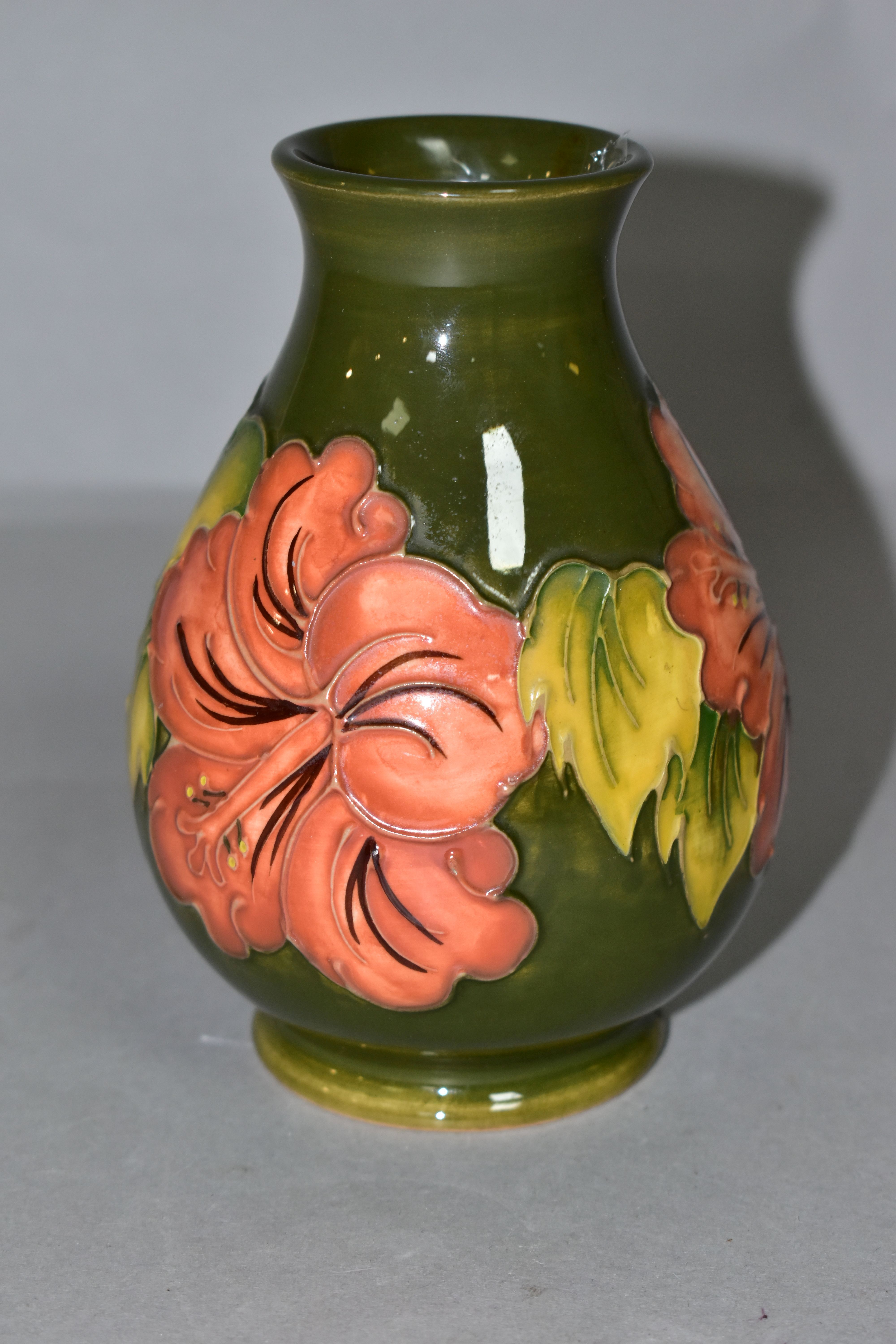 A MOORCROFT POTTERY BALUSTER VASE DECORATED WITH CORAL HIBISCUS ON A GREEN GROUND, impressed marks