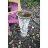 A COMPOSITE BIRD BATH in the form of three winged cherubs standing on a column holding the bowl