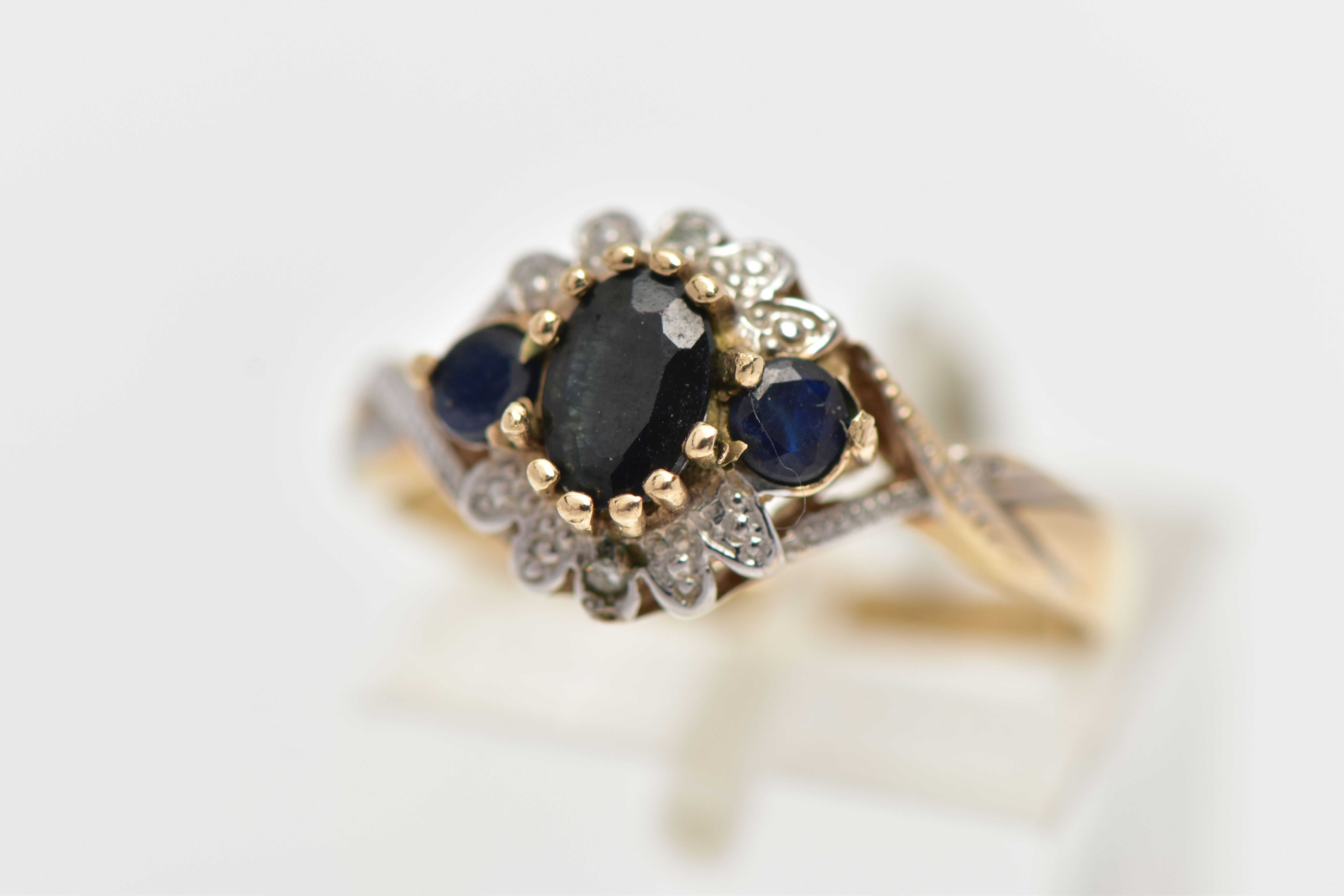 A 9CT GOLD CLUSTER RING, of a circular form, set with an oval and two circular cut blue sapphires,