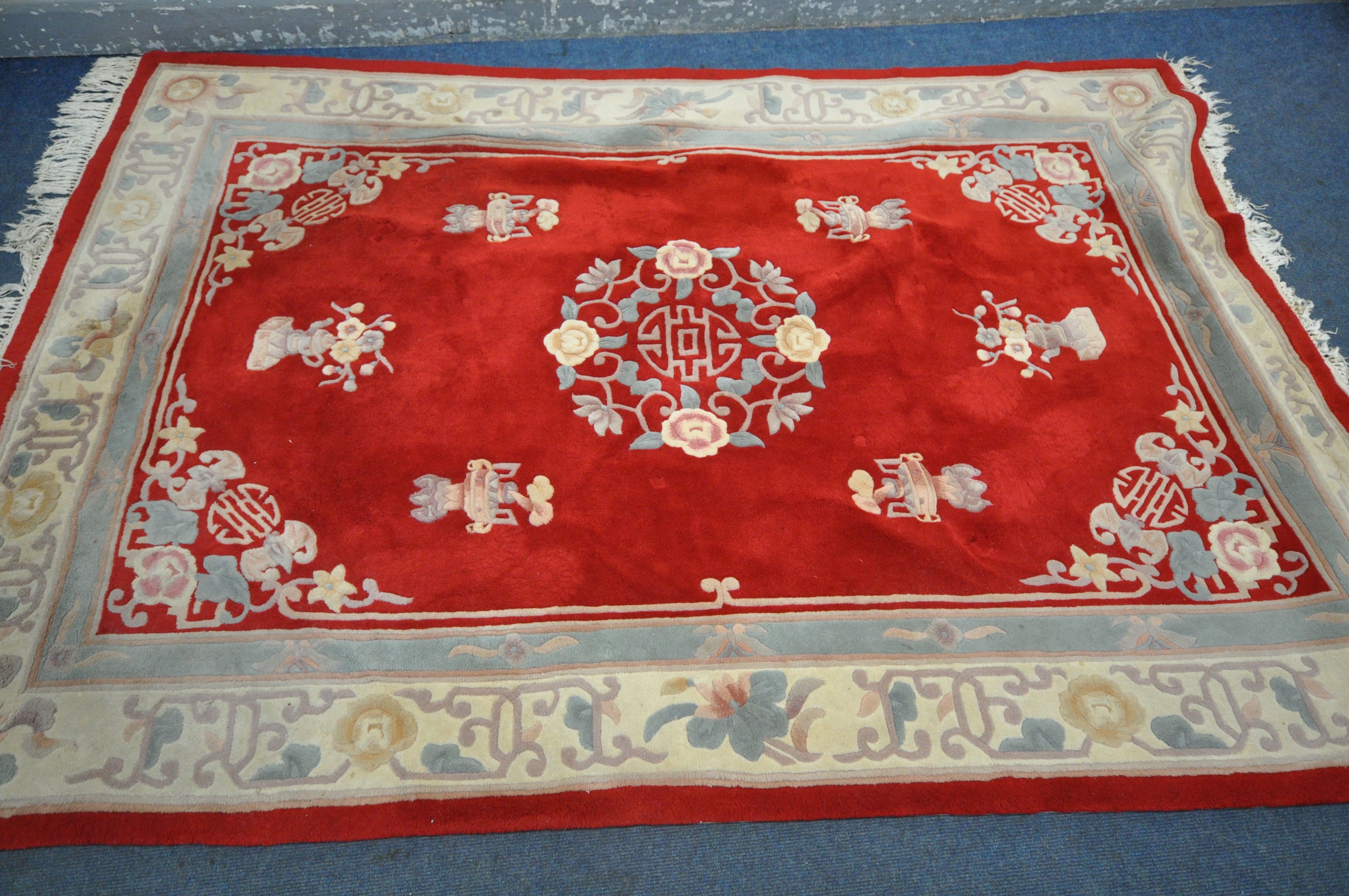 A RED GROUND WOOLEN RUG, with a multi strap border, and a central floral design 276cm x 190cm (