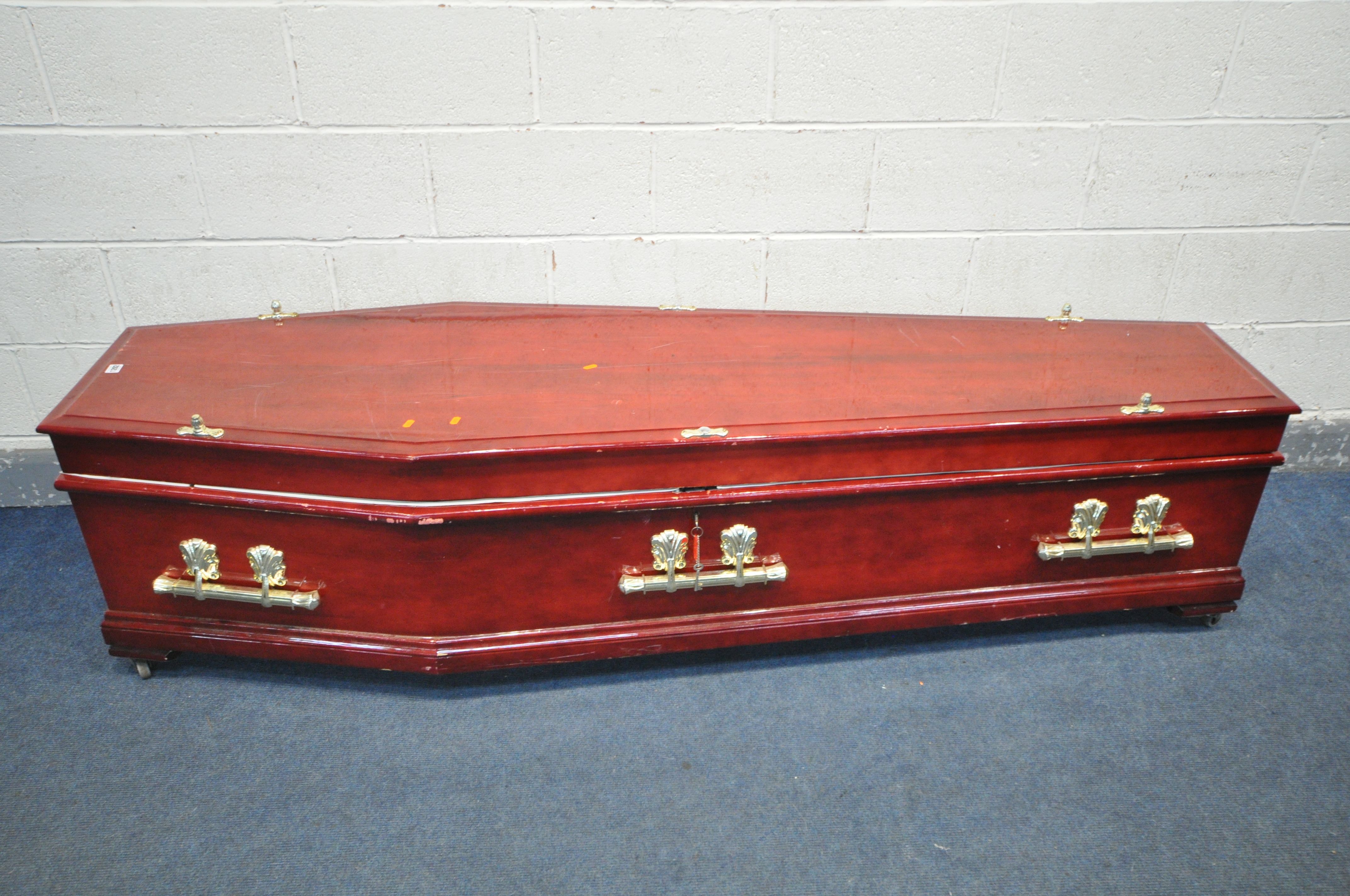 A BESPOKE COFFIN, with a glossy red finish, plastic finials and handles, length 211cm x depth 62cm x