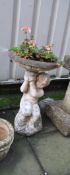 A MODERN COMPOSITE BIRD BATH in the form of a Cherub holding the bowl aloft 63cm high (planted