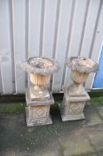 A PAIR OF COMPOSITE GARDEN URNS with acanthus leaf detailing to urn standing on square columns