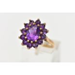 A 9CT GOLD AMETHYST CLUSTER RING, of an oval form, set with a central oval cut amethyst within a