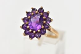 A 9CT GOLD AMETHYST CLUSTER RING, of an oval form, set with a central oval cut amethyst within a