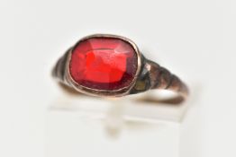 A YELLOW METAL GEM SET RING, set with an oval cut red stone assessed as paste, collet set in a