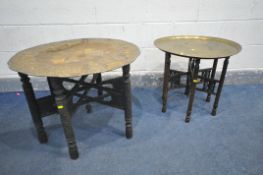 AN ANTIQUE HEAVILY CARVED FOLDING TABLE, with a circular beaten brass top, diameter 75cm x height