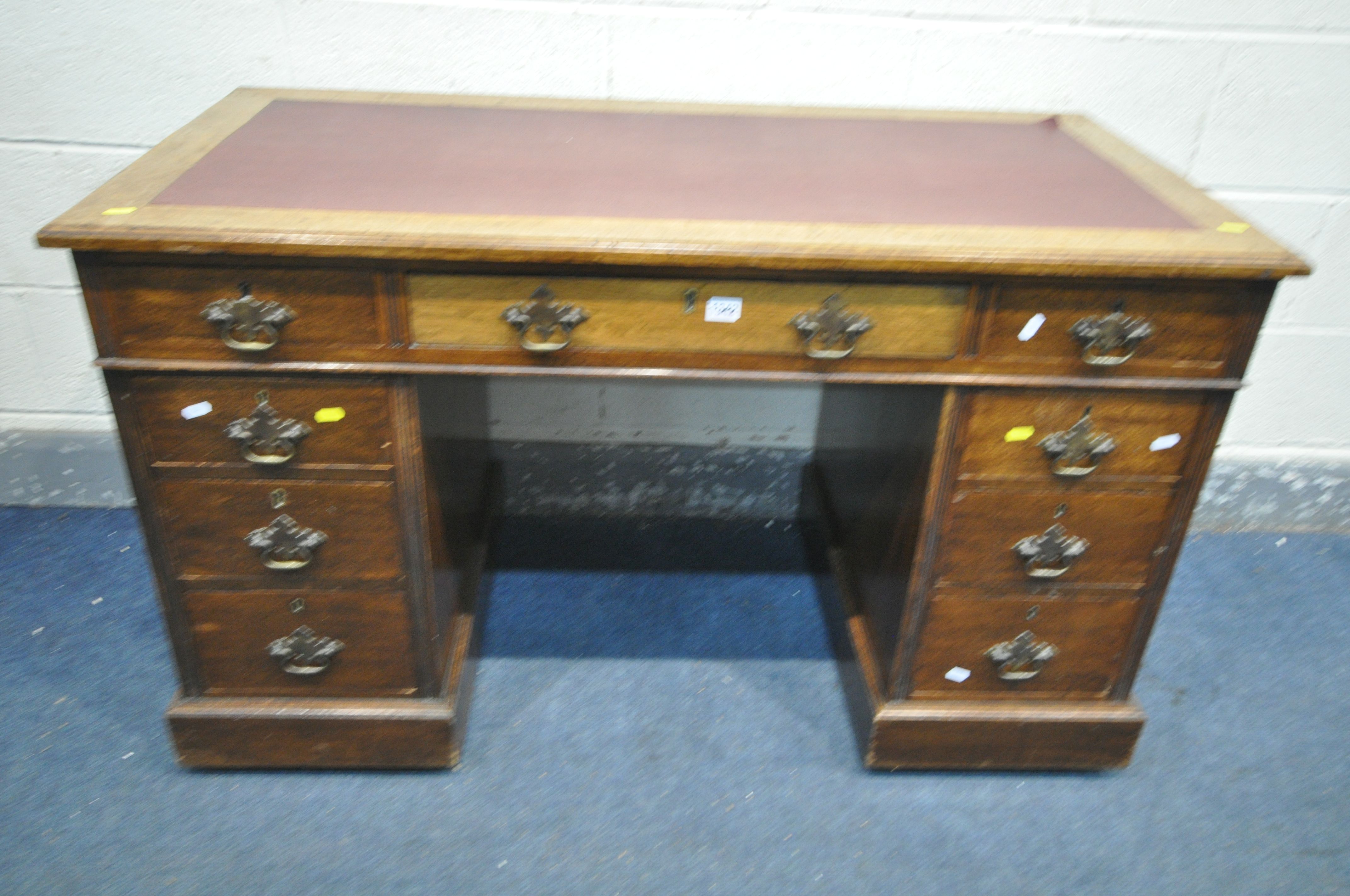 AN EDWARDIAN OAK PEDESTAL DESK, with burgundy leatherette writing surface, and nine various drawers,