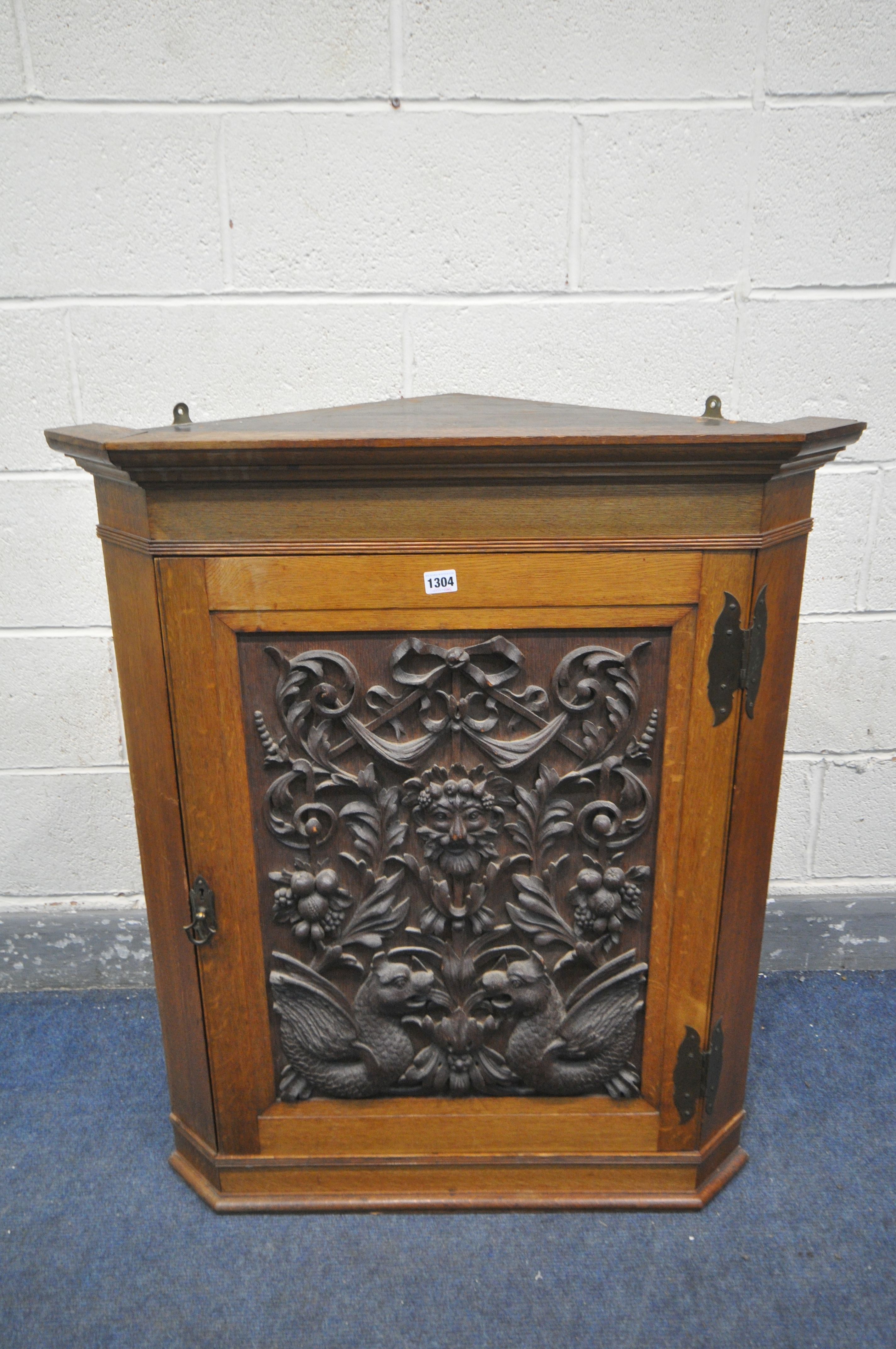 A 20TH CENTURY OAK HANDING CORNER CUPBOARD, with a heavily carved foliate panel, a depicting a