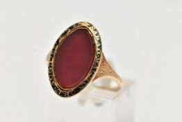A YELLOW METAL AND CARNELIAN MOURNING RING, of an oval form, set with a central oval cut polished