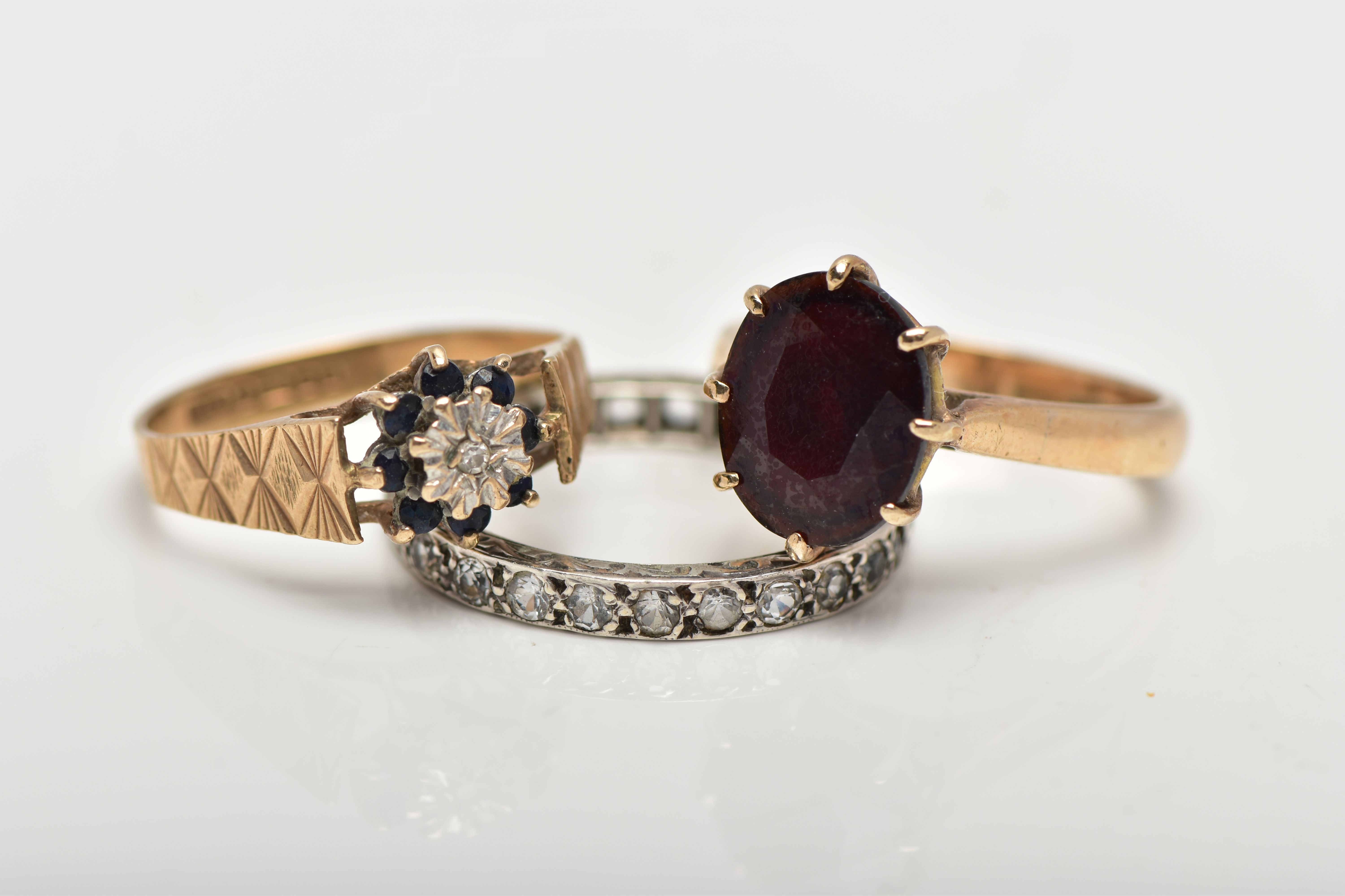 THREE GEM SET RINGS, the first designed with an oval cut garnet in an eight claw setting with