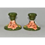 A PAIR OF MOORCROFT POTTERY SQUAT CANDLESTICKS, in Coral Hibiscus pattern on a green ground,