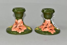 A PAIR OF MOORCROFT POTTERY SQUAT CANDLESTICKS, in Coral Hibiscus pattern on a green ground,