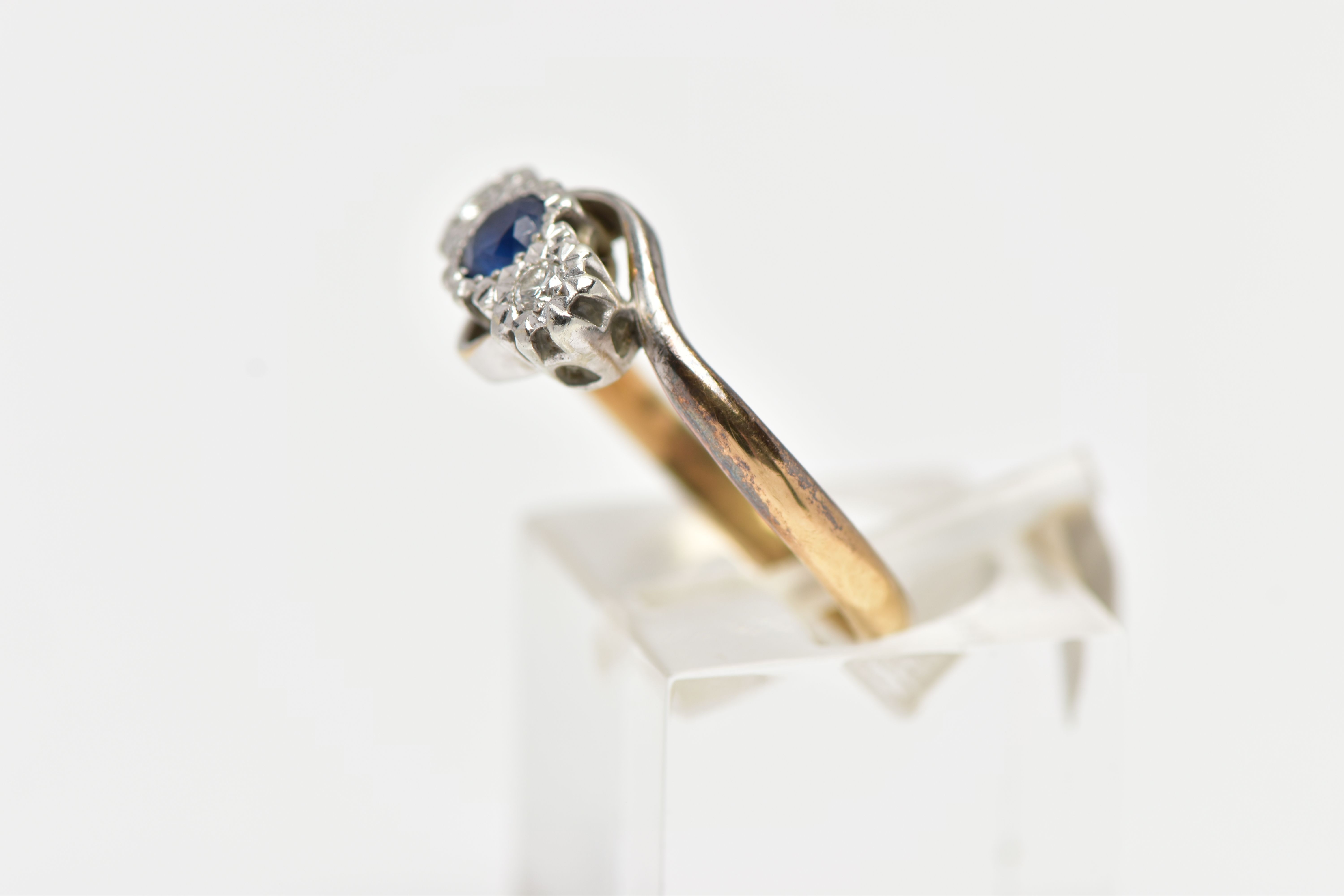 A YELLOW METAL CROSS OVER THREE STONE RING, designed with a central circular cut blue sapphire, - Image 2 of 4