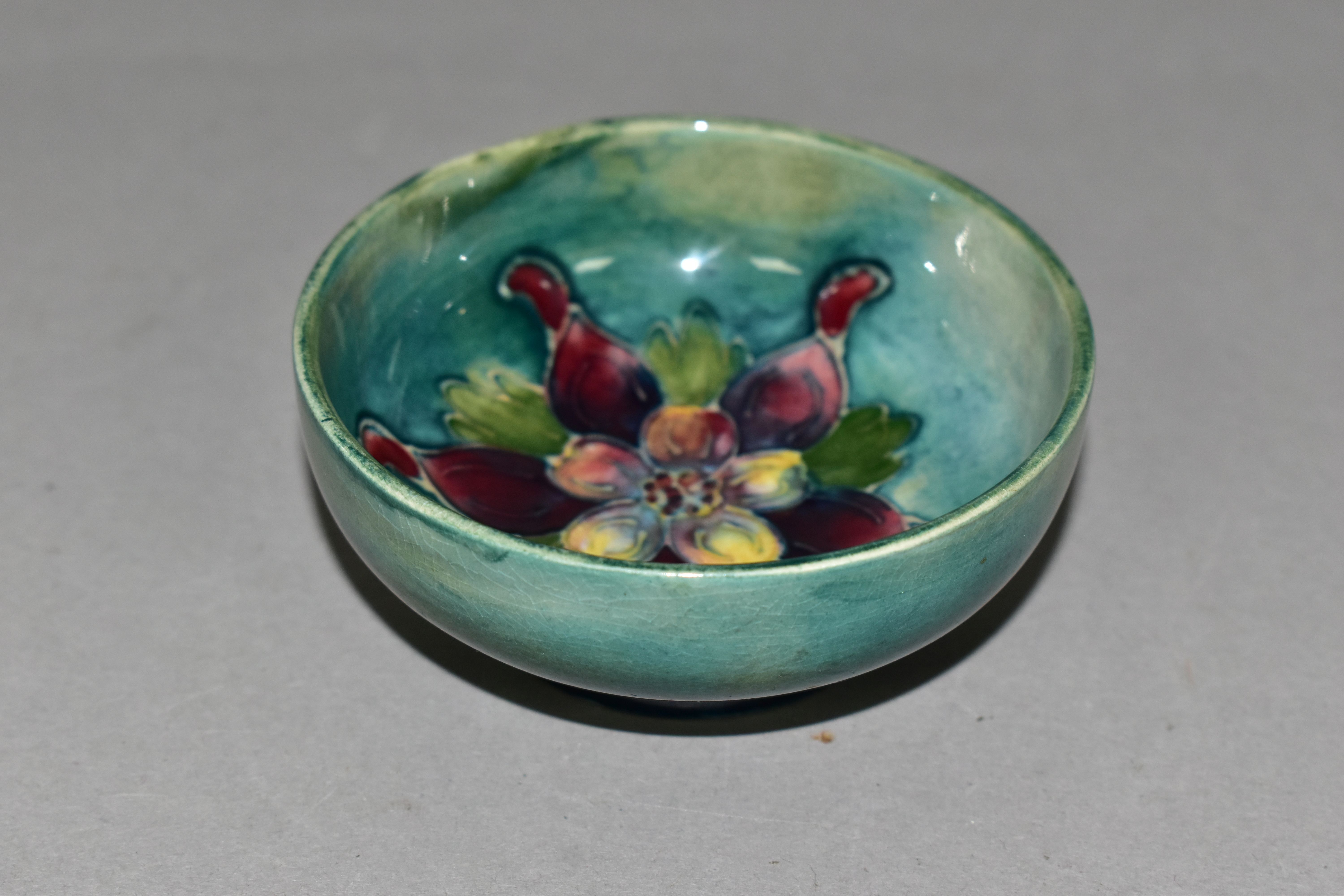 A SMALL MOORCROFT POTTERY FOOTED BOWL, 'Columbine' pattern on blue/green ground, impressed marks